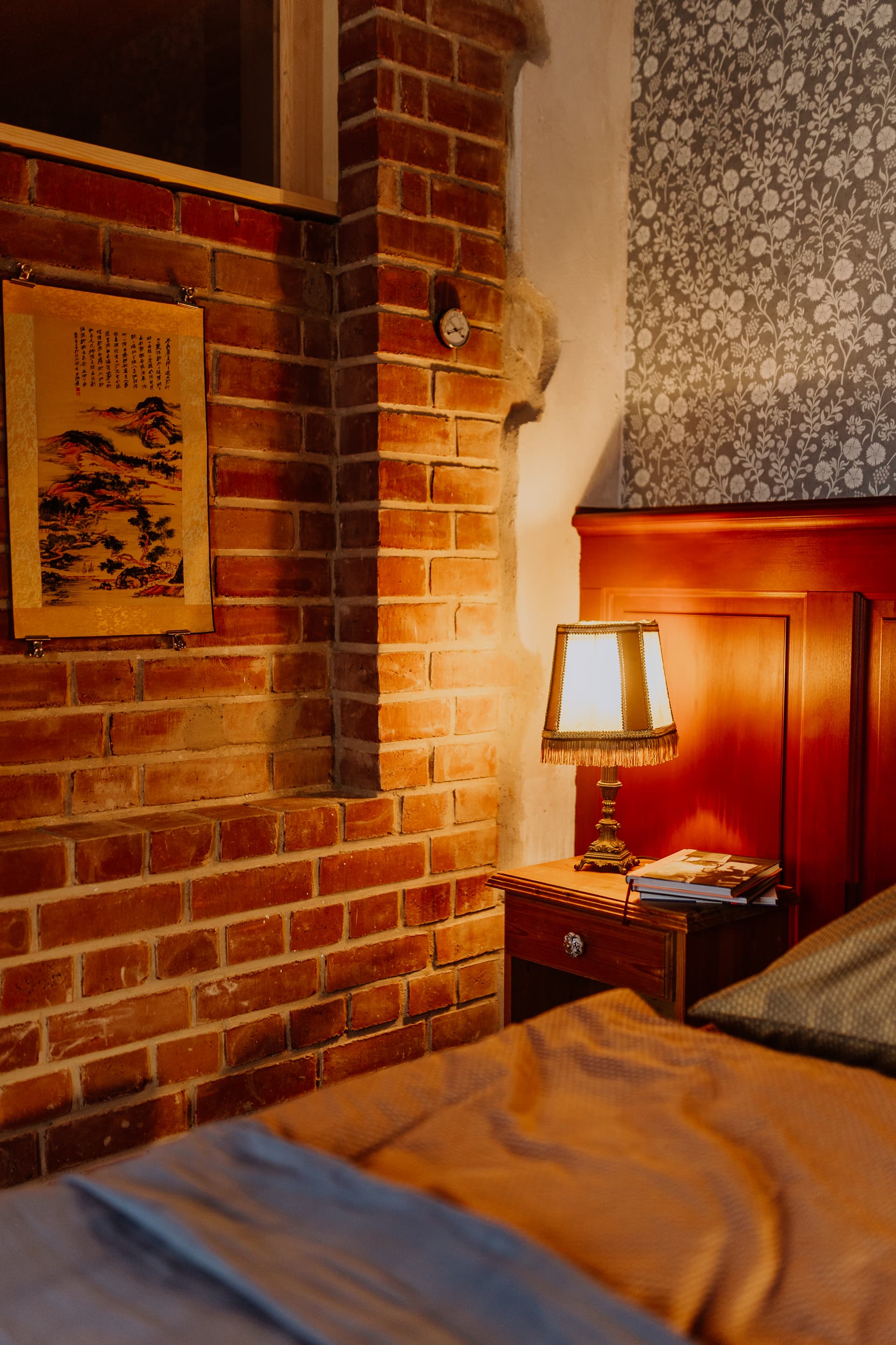 Schlafzimmer im Erdgeschoss mit Doppelbett, Fransen-Nachttischlampe, Ziegelwand und floraler Akzenttapete