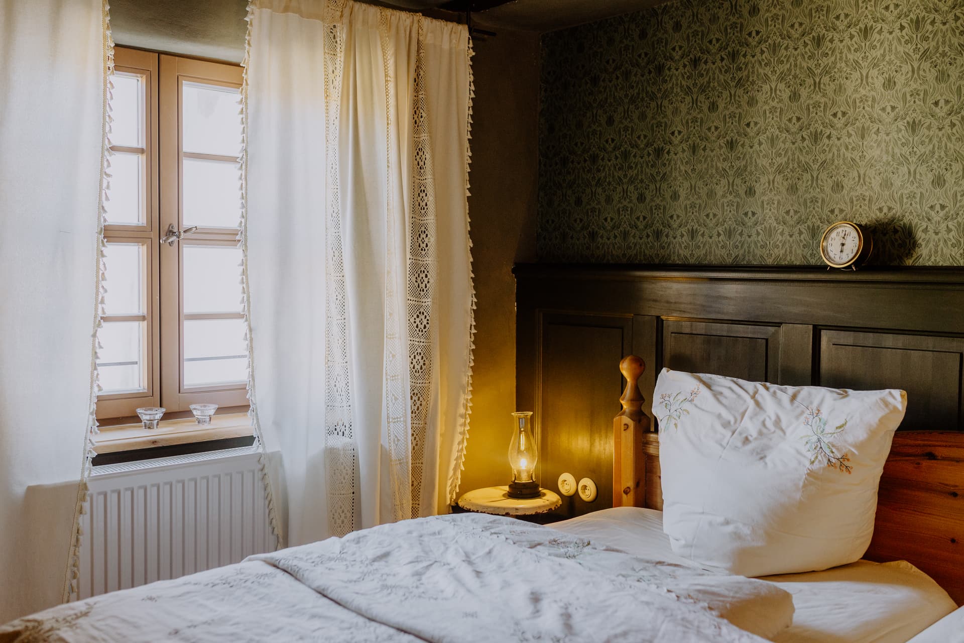 Hauptschlafzimmer im Obergeschoss mit Holzbett, weißer Leinenwäsche, dunkelgrüner Kassettenvertäfelung und Mustertapete
