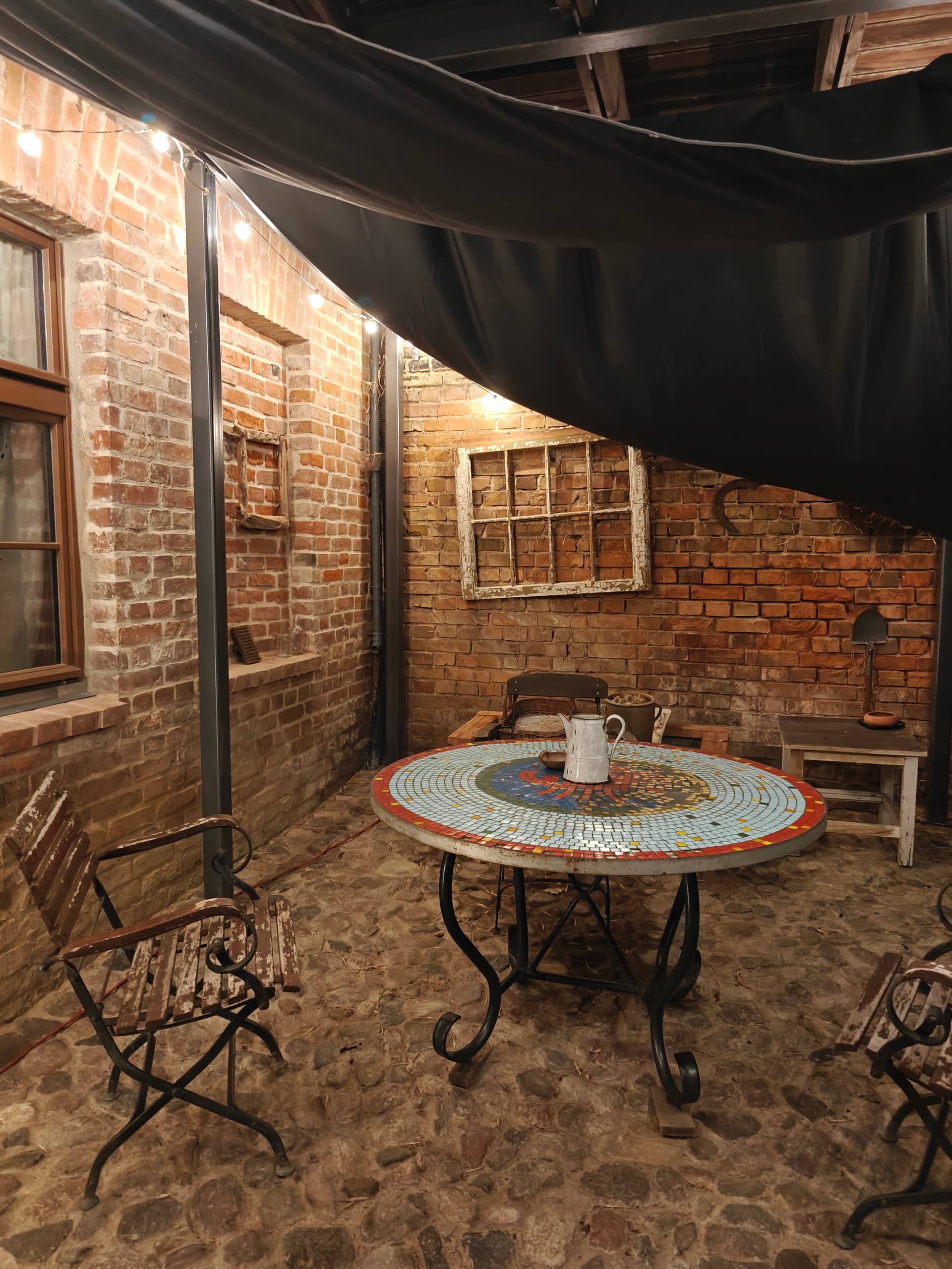 Überdachte Hofterrasse mit historischem Feldsteinpflaster, Mosaiktisch, Gartenstühlen und Baldachin mit Lichterkette