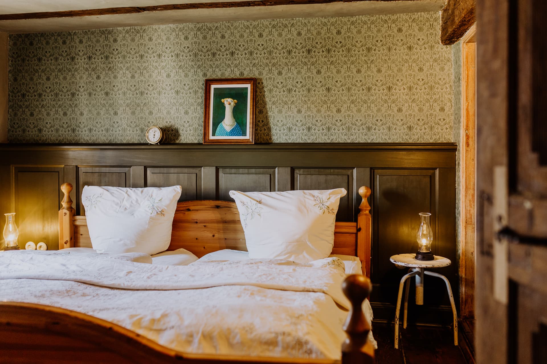 Schlafzimmer mit Doppelbett, weißer Leinenwäsche, dunkelgrüner Kassettenvertäfelung und botanischer Tapete