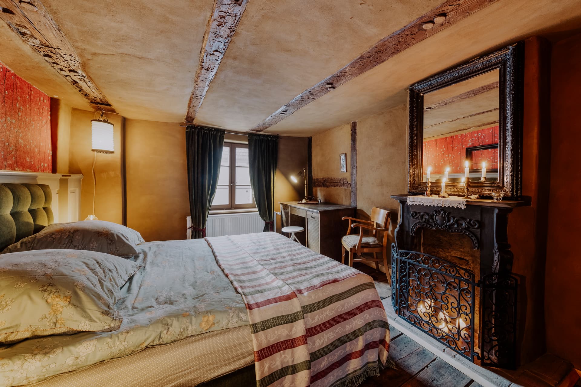 Großes Schlafzimmer mit Doppelbett, Holzbalkendecke, gusseisernem Kerzenkamin, antikem Spiegel und Schreibtisch